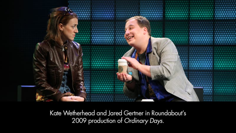 Kate Wetherhead and Jared Gertner in Ordinary Days. A light-skinned woman with short, brown hair held back by a pair of large sunglasses looks at a light-skinned man who leans forward, holding coffee.