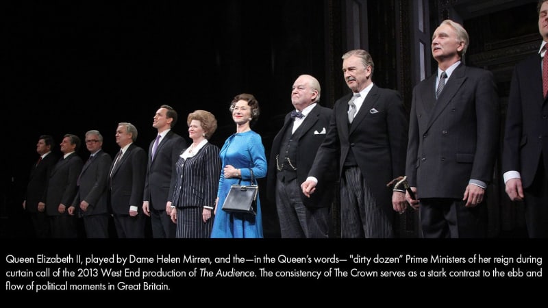 An older, light-skinned woman in a blue dress stands in the center of a long row of light-skinned men in black suits