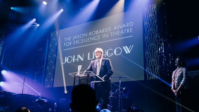 John Lithgow stands at a podium accepting the Jason Robards Award for Excellence in Theatre.