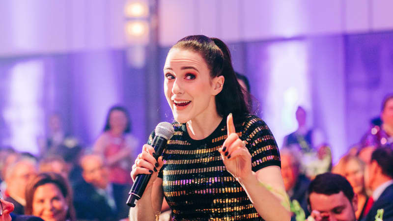 Rachel Brosnahan holds a microphone and speaks to a crowded Ziegfeld Ballroom.