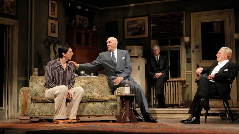 The cast of Man and Boy on stage. Two men are sitting on a couch while one sits to the right on a chair and one stand far in the background. 