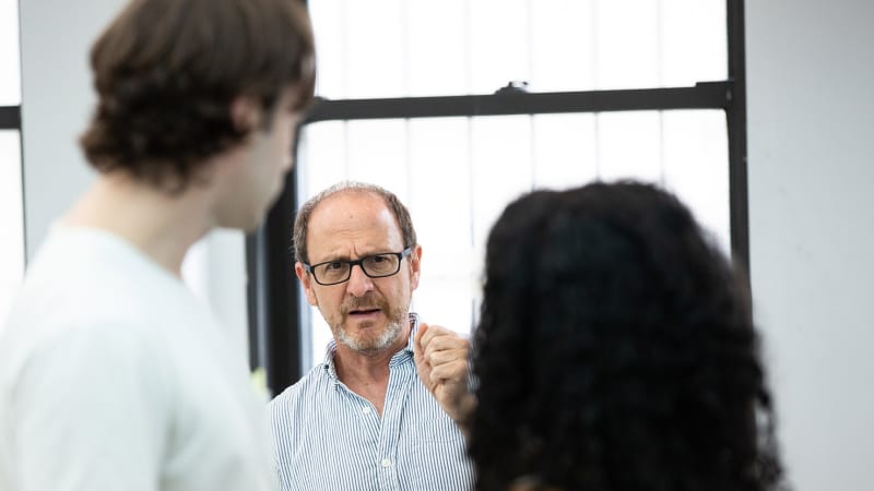 Blurred in the foreground are two actors, and in between them in the background, in focus, is the director giving them a note.