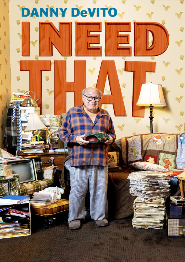 Danny DeVito standing in a room filled with miscellaneous items all over the place and the title "I Need That" in bold orange text on the well behind him.