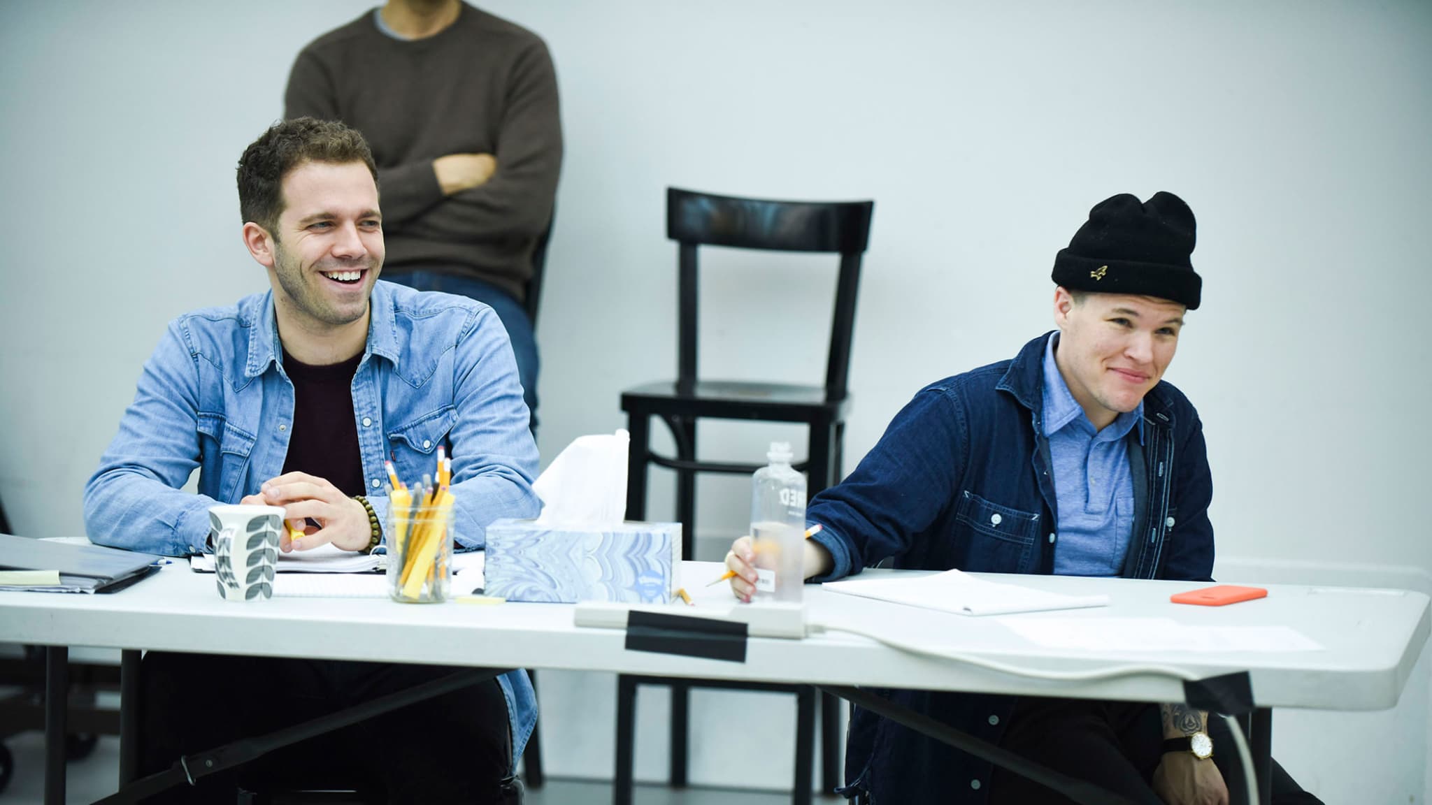 Alex Lubischer and Will Davis smile and sit behind a white table in rehearsals for BOBBIE CLEARLY.