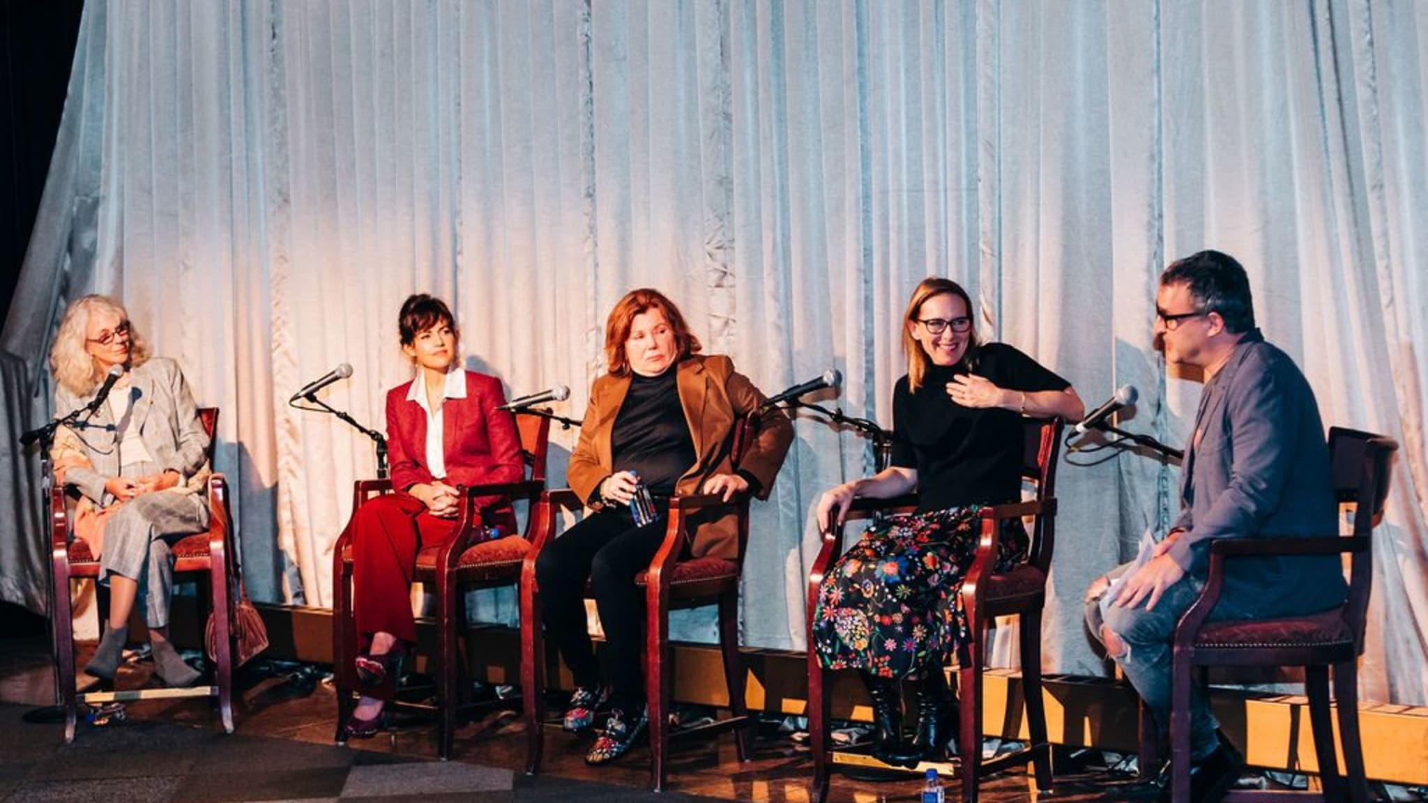 Five people talking in a panel sit in chairs with microphones in front of them.