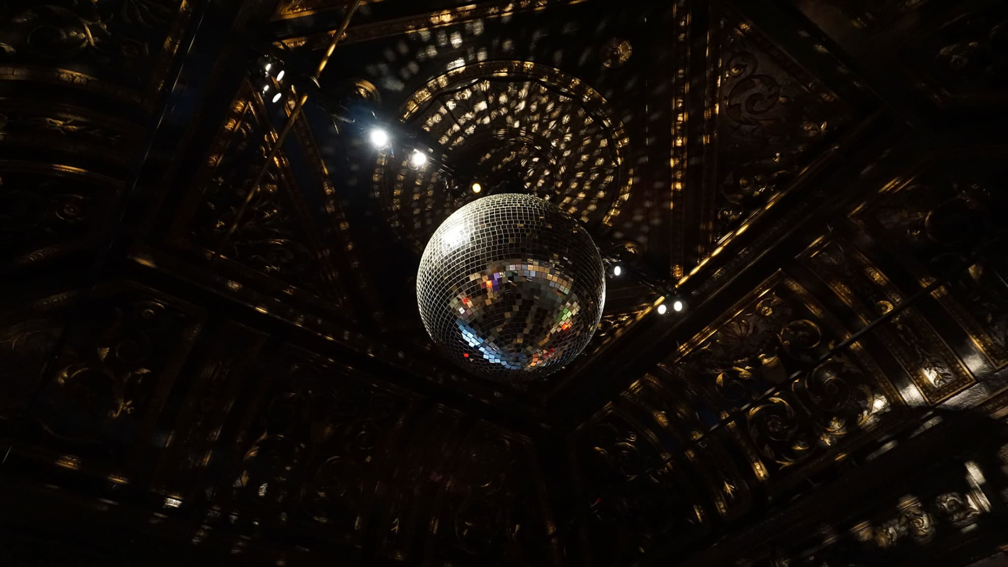 A large mirror ball creates numerous spots of light around a dark room.