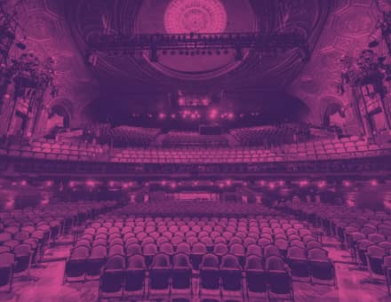 The empty house of Studio 54. The floor of the orchestra section is wooden. Elaborate gold moldings are on the red walls and ceilings, with a bright blue and gold dome at the top.