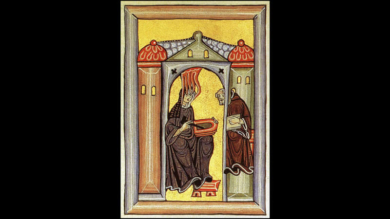 A nun sits, feet on a stool, holding a round red object. She faces a man in a brown monk’s habit. Four red tentacles reach down from the ceiling and rest on her forehead.