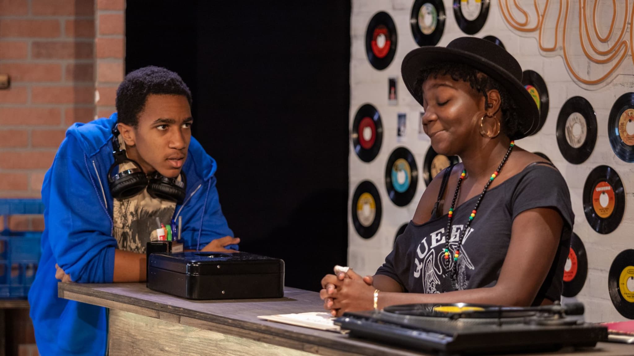 Two students by a counter with records behind them during the RYE production of GROOVES.