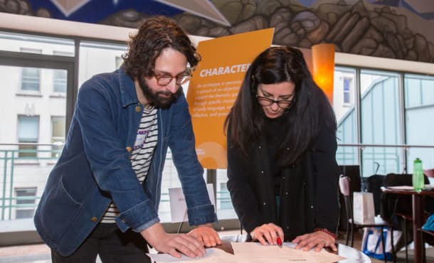 Two people stand over a table looking at paperwork in the American Airlines penthouse lobby. Behind them is a poster board titled CHARACTER.