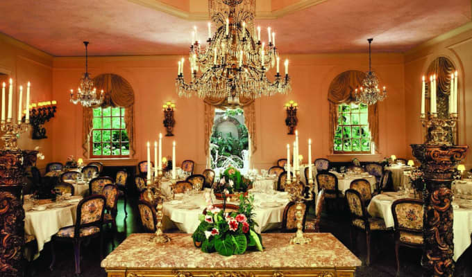 A very fancy dining room with several tables, varying sizes of chandeliers, and tall candlesticks.