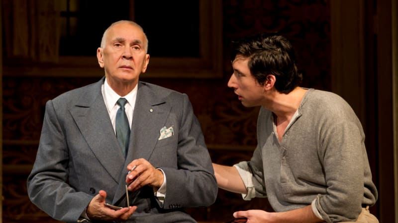 two men sitting down. the younger man is leaning in to say something to the older man in a suit. 