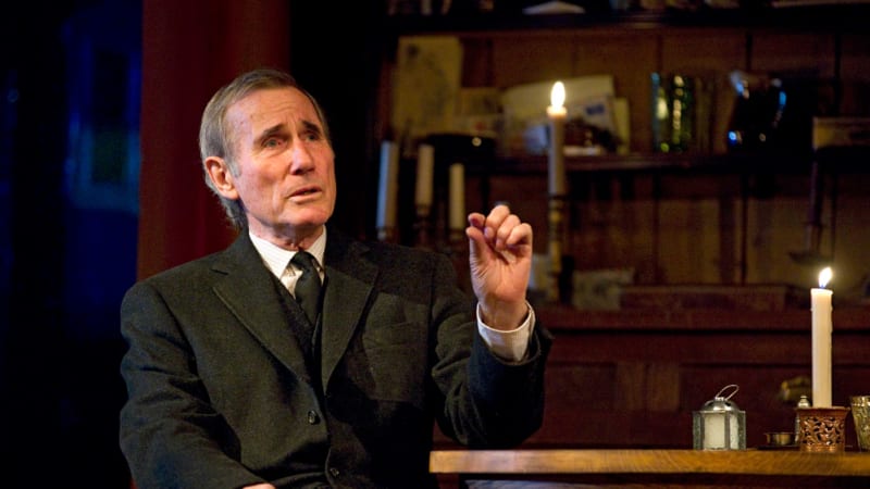A man in a suit sitting at a table in candle light. 