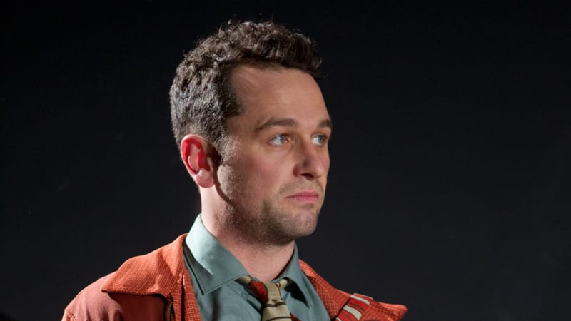 A man is standing with a paper in his hands while he stares off. 