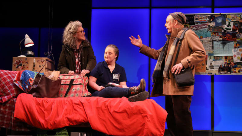 A woman with Down syndrome sits on a bed full of bags while an older couple stands on either side of her in a heated conversation.