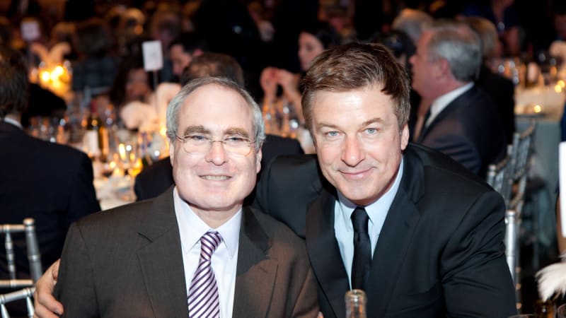 Todd Haimes and Alec Baldwin lean in for a photo at a formal dining table.