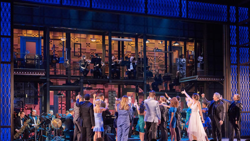 The cast of MY ONE AND ONLY at curtain call. Everyone turns to the back of the stage and gestures towards the orchestra up high on platforms.