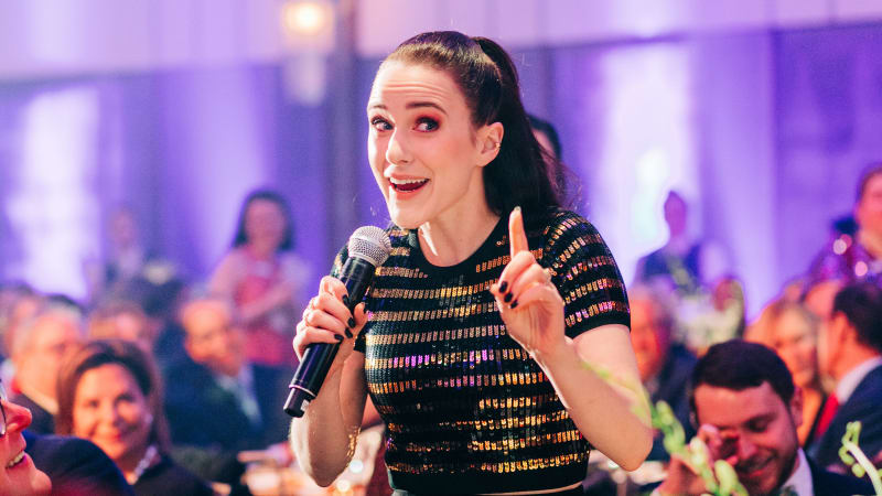 Rachel Brosnahan holds a microphone and speaks to a crowded Ziegfeld Ballroom.