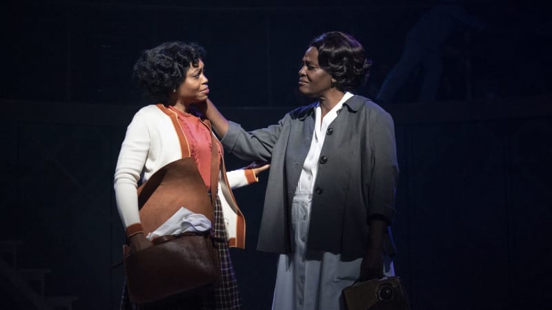 Two Black women look at each other with sadness, like they're saying goodbye. One touches the other's face, the other touches the other's arm.