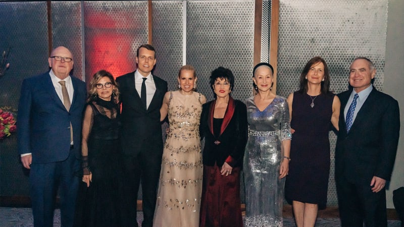 A group of people dressed in formal clothes smile in the Ziegfeld Ballroom for a photo.