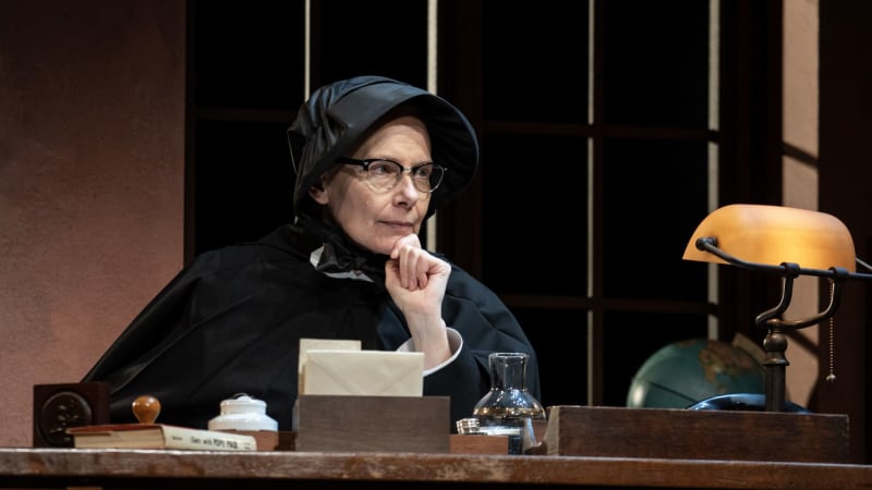 A nun sitting behind a desk with her hand to her chin. 