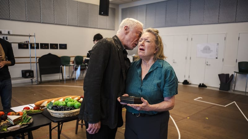 A man whispers into the ear of a woman who has a pained expression and holds a small wooden box.