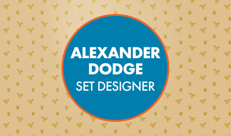 "Alexander Dodge Set Designer" written in white text in a blue circle with an orange frame. The circle is in front of floral wall paper background.