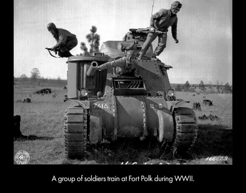 A tank, with large, rotating metal belts at the bottom, and forward-facing guns on the left side and top. Two soldiers stand on the roof, poised to jump, holding guns. A third soldier is half out of a