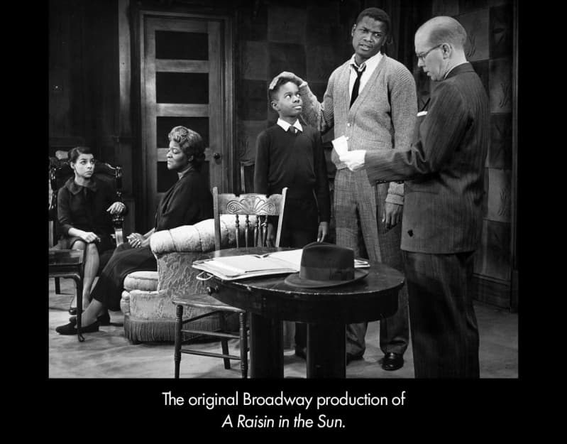The original Broadway production of A RAISIN IN THE SUN. In a living room, a white man in a suit looks at a piece of paper as a Black man and boy look on. Two seated Black women also look at them.