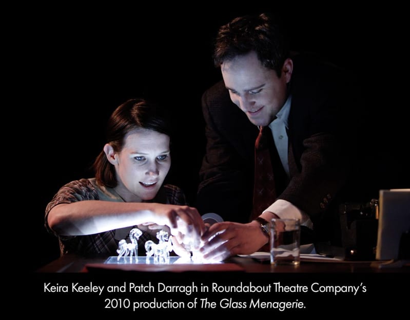 Keira Keeley and Patch Darragh in our 2010 production of THE GLASS MENAGERIE. A light-skinned woman and man place their hands on a few glass horse figurines with a ligh below them making them glow.