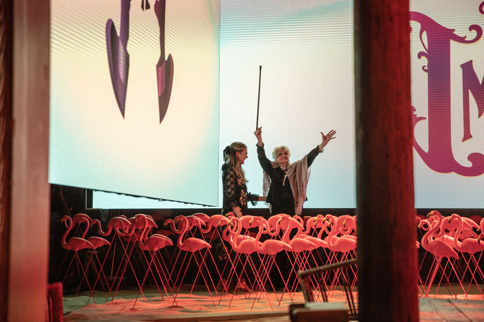 Lily Rabe and Angela Lansbury, who holds her arms up while holding a can, stand on stage behind a bunch of pink flamingo lawn decorations from THE ROSE TATTOO. Photo by Evan Zimmerman.