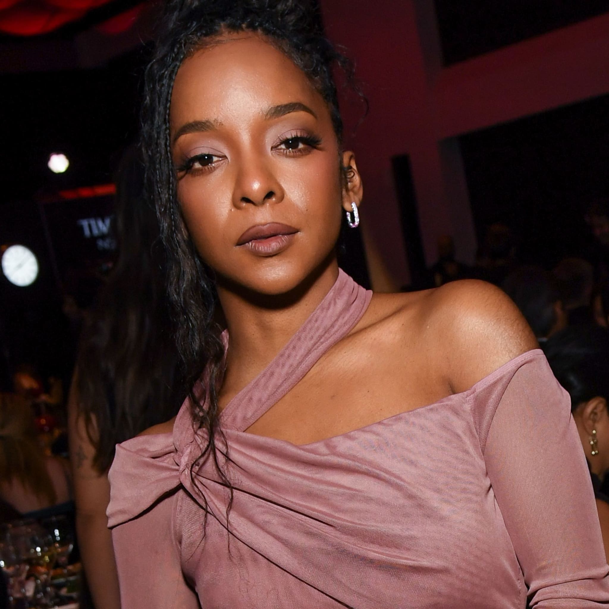 Kara Young has a medium-dark skin tone, dark brown eyes with glam eyeshadow, and wears her braided hair in a fancy updo. She also wears an off the shoulder, muted pink dress.