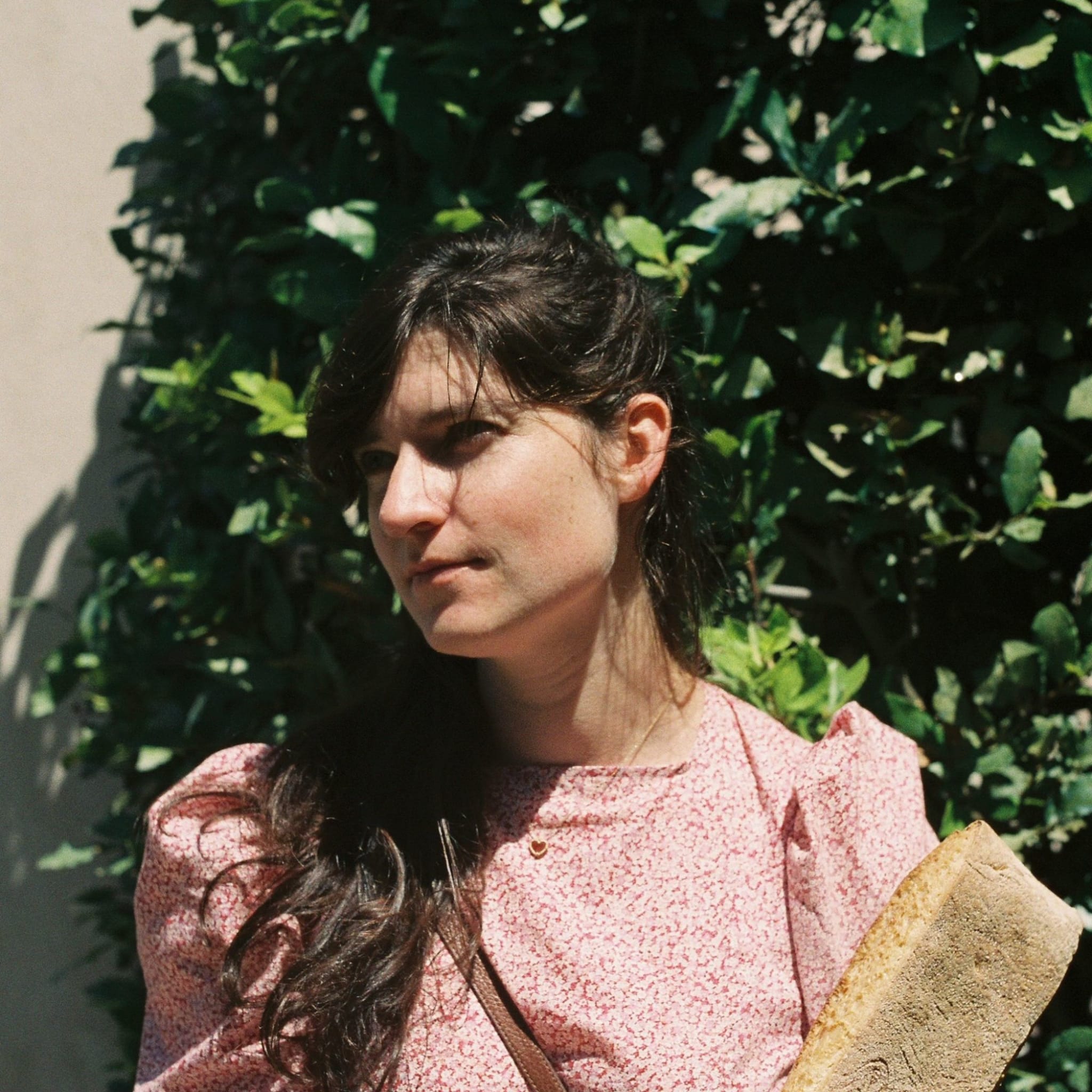 Liba has light skin, long, dark brown hair cascading over one shoulder, and wears a light pink blouse.