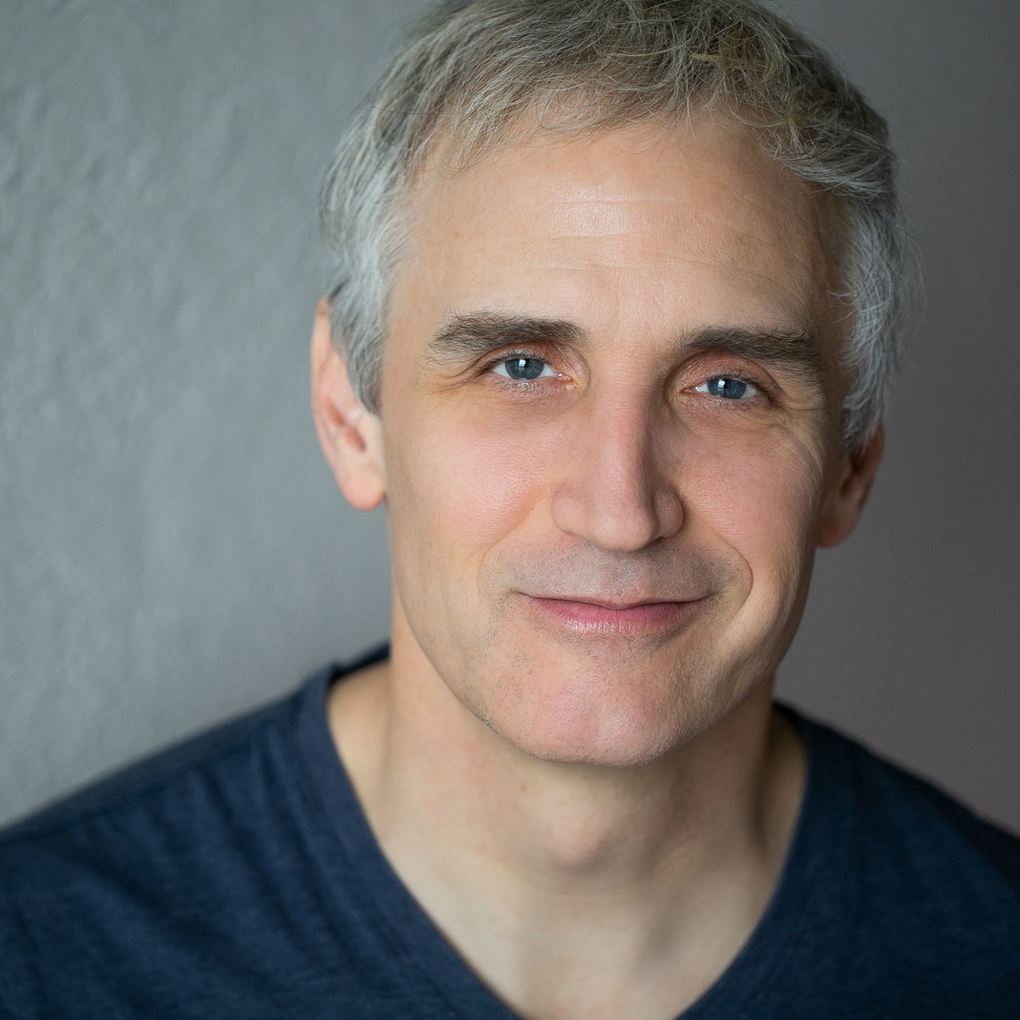 Pete has light skin, blue-gray eyes, short gray hair, a clean-shaven face, and wears a dark blue t-shirt.