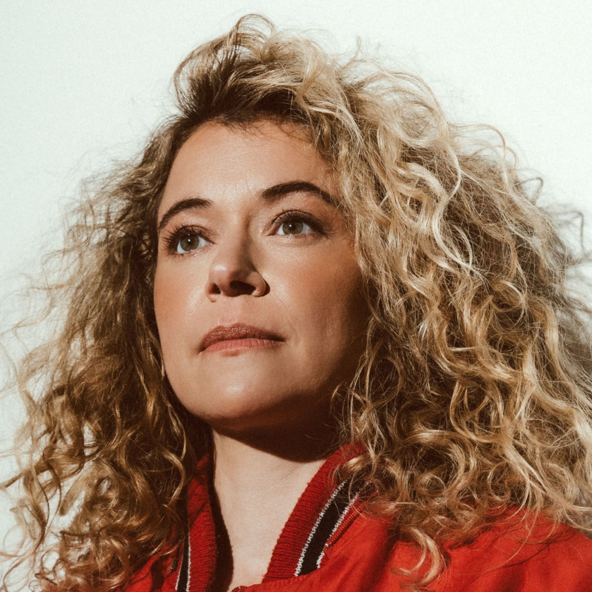 A photo of Tatiana Maslany. A woman with curly blonde hair, wearing a red top.