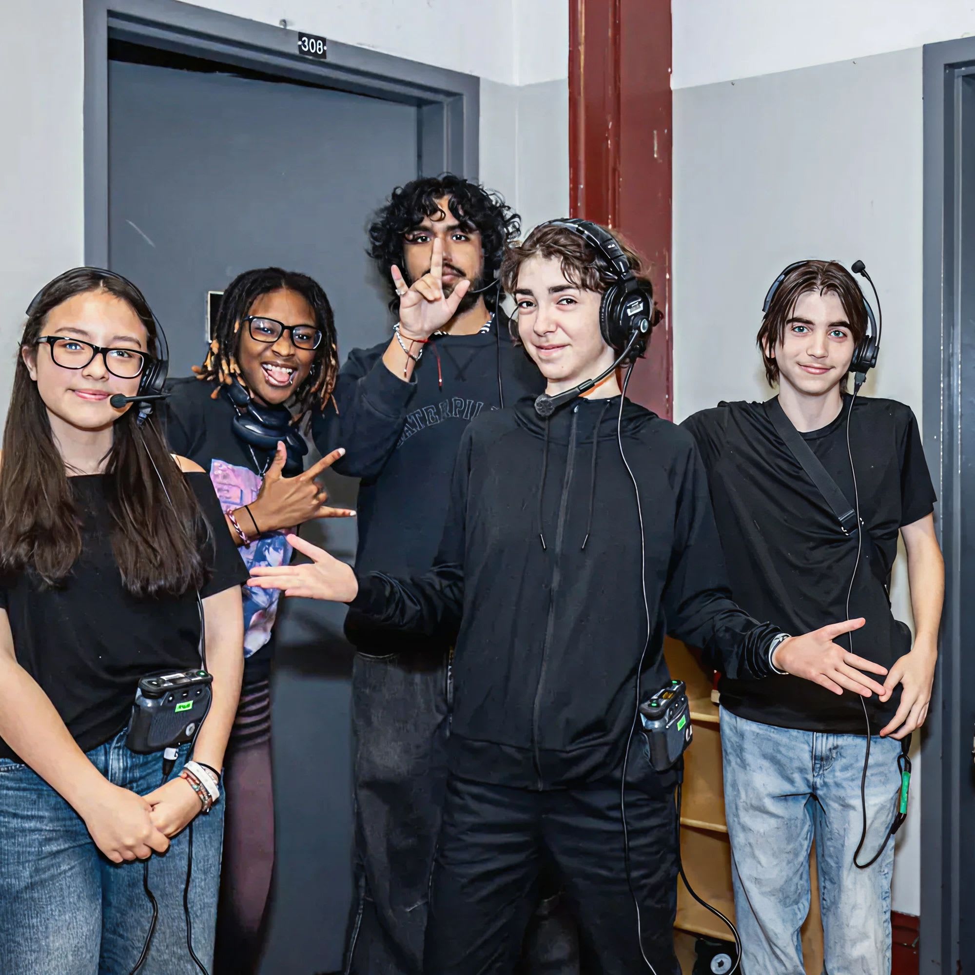 Members of the Roundabout Youth Ensemble stand backstage wearing headsets, preparing to support a theatre production.