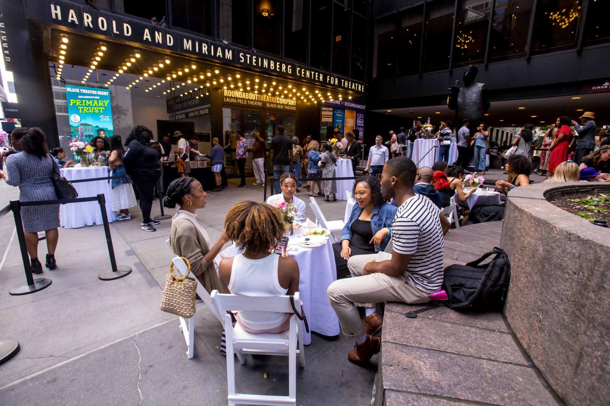 Guests dine and mingle at outdoor tables during a Black Theatre Night reception for Primary Trust outside the Harold and Miriam Steinberg Center for Theatre at Roundabout Theatre Company.