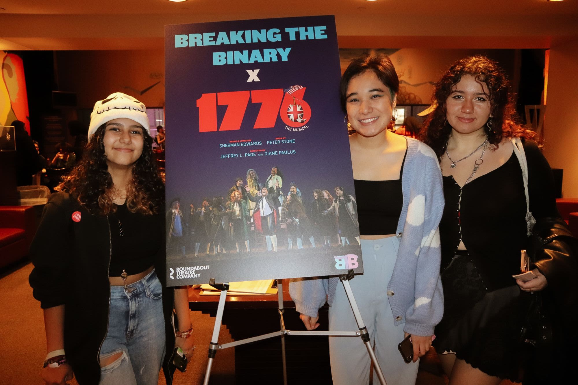 Three guests pose beside a Breaking the Binary × 1776 event poster at a Roundabout Theatre Company community night.

