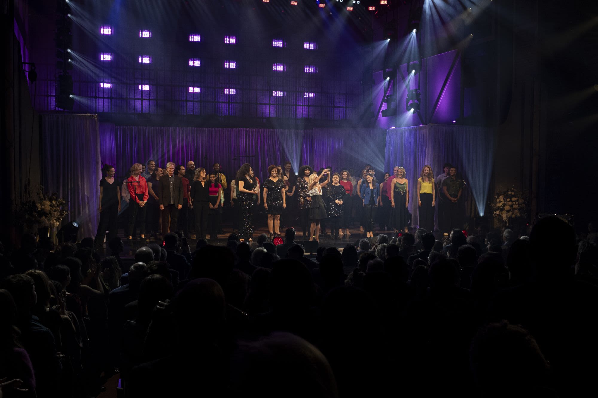 A group of performers all on stage under the lights bowing to the crowd and thanking them.