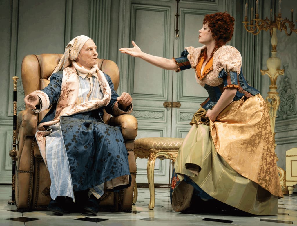 Actors Bill Irwin and Rachel Bloom are sat together and wear colorful costumes on stage.