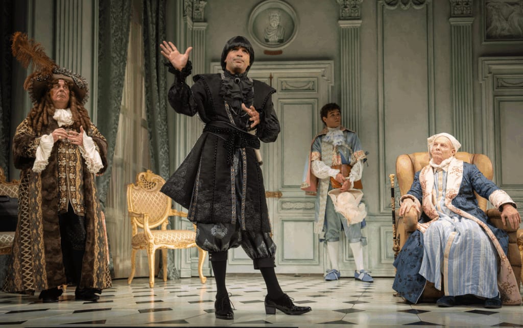 Actors on stage in colorful period piece costumes.