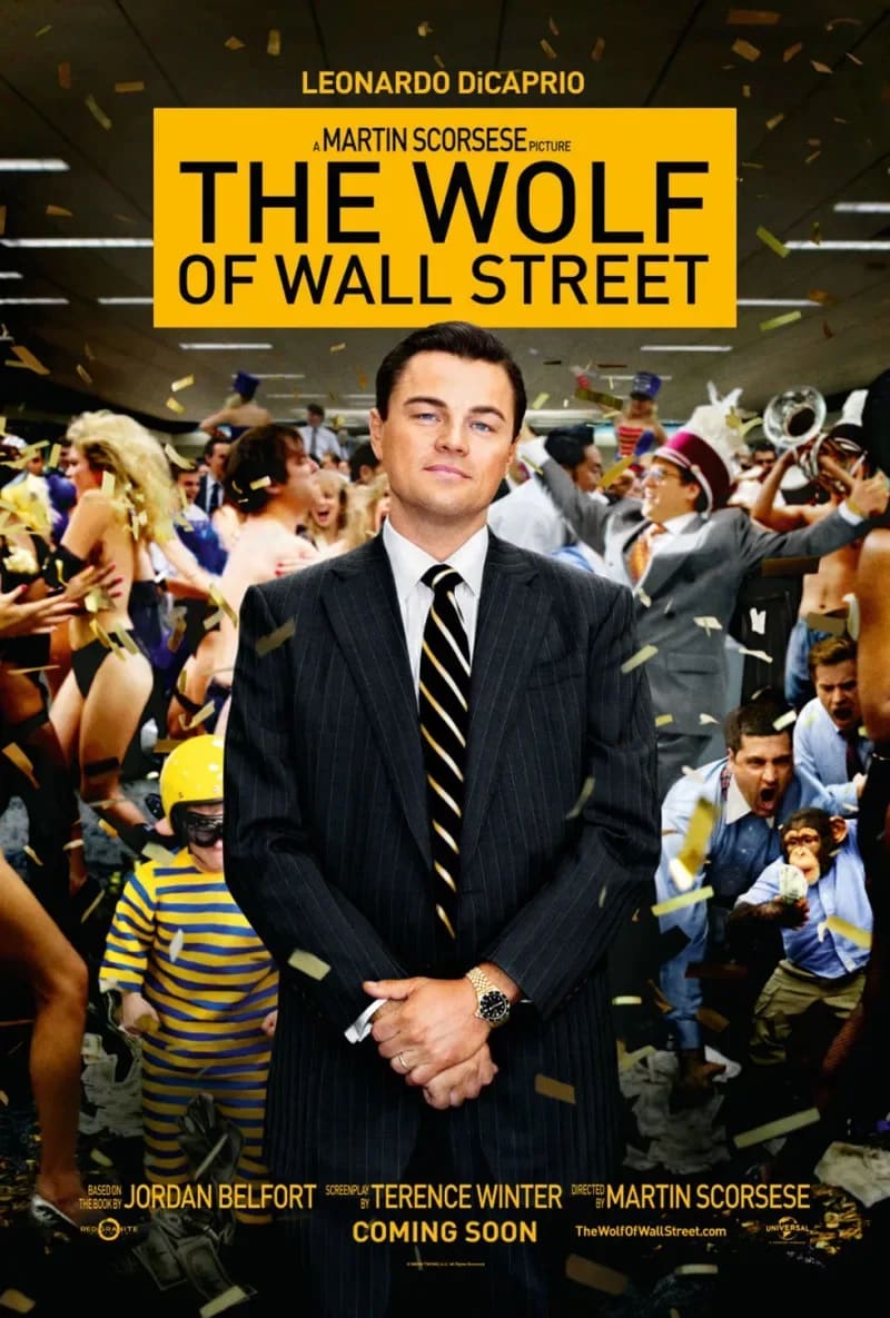 A young, light-skinned man in a dark suit stands in front of a chaotic frenzy of people and confetti in an office setting.