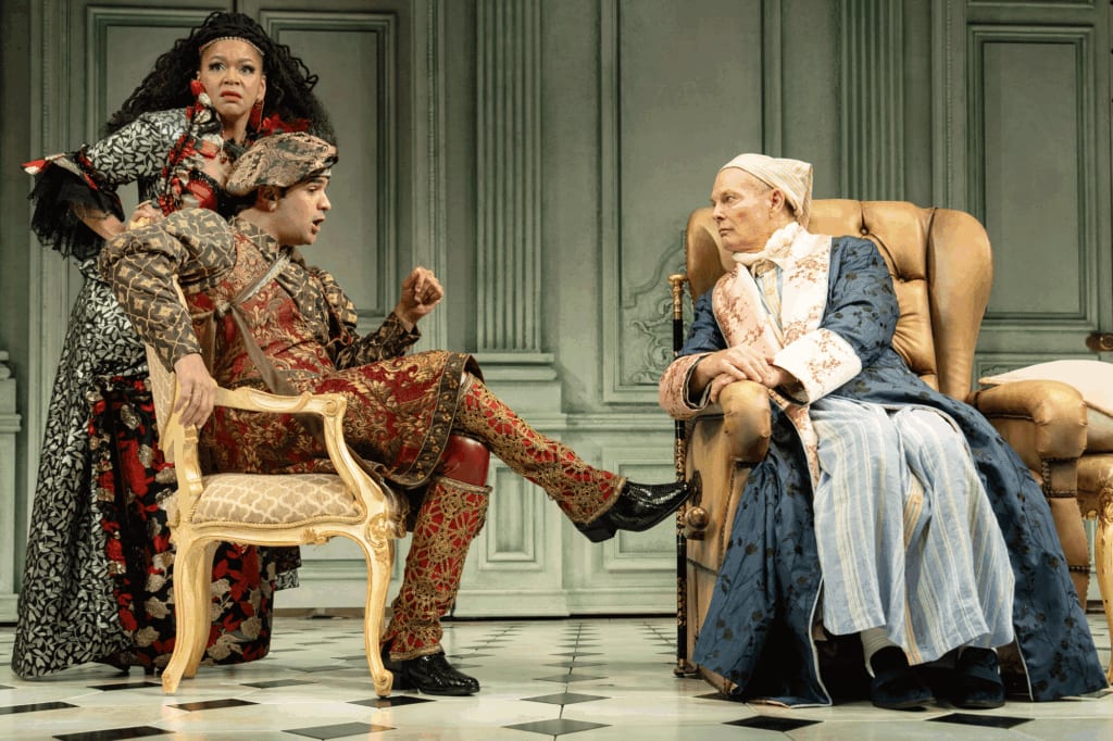 Three actors in conversation on an ornate stage in colorful period piece costumes.
