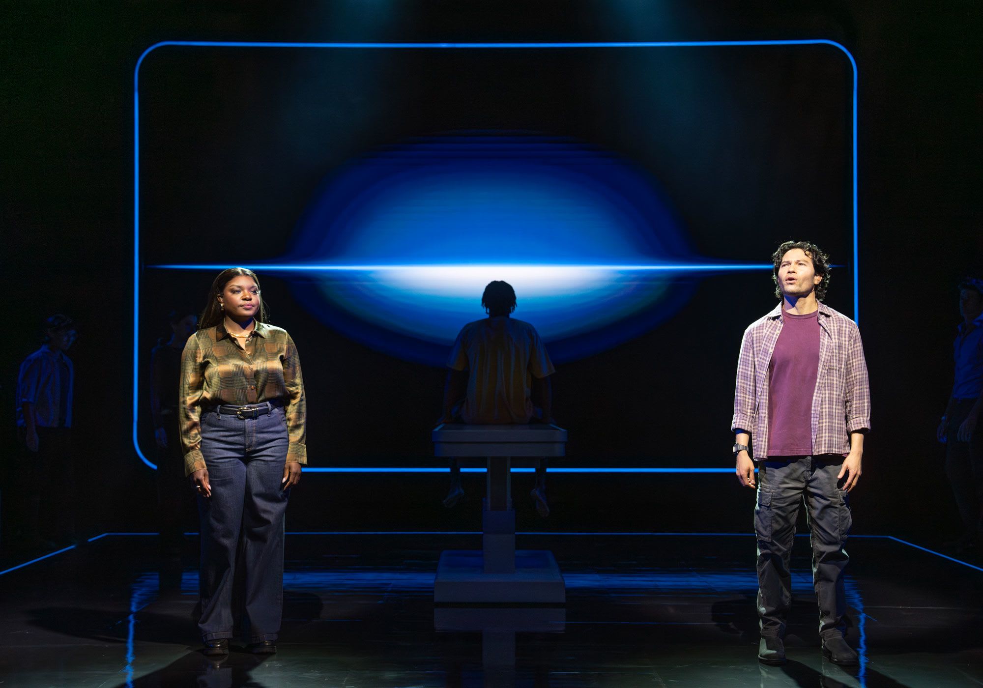 Two actors onstage singing with an operating table in the background.