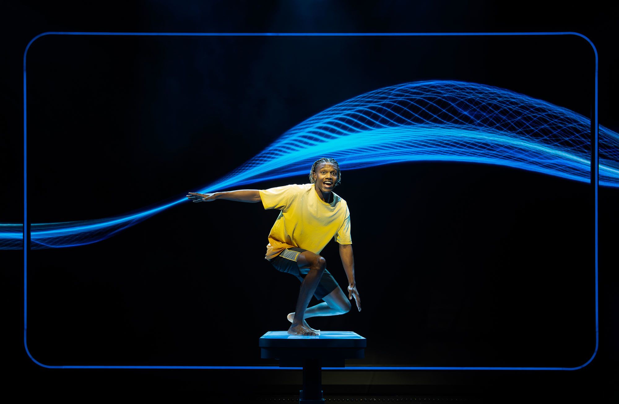 Actor surfing in front of a video depicting a wave.