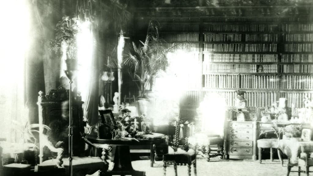 A high-ceiling library, the back wall covered in books. Two tall windows let light in from the left. A faint, ghostly figure of a person sits in a chair.