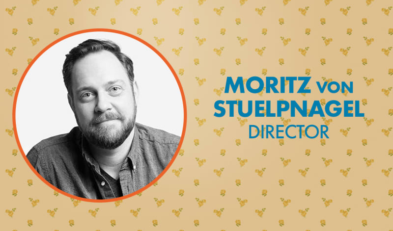 Black and white headshot of Moritz von Stupnegal in an orange frame and a floral wallpaper background. 