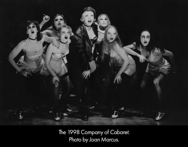 Black and white photo of the 1998 company of CABARET. A group of women in risque silk lingerie and tights sing together in clump.