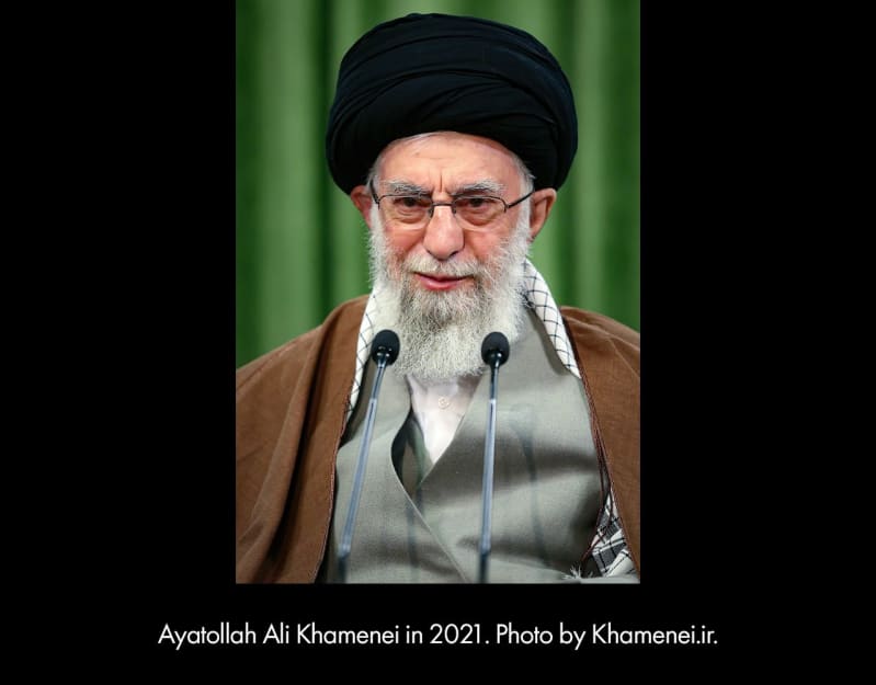 Ayatollah Ali Khamenei in 2021. An older, light-skinned man in a black head wrap speaks into two microphones.