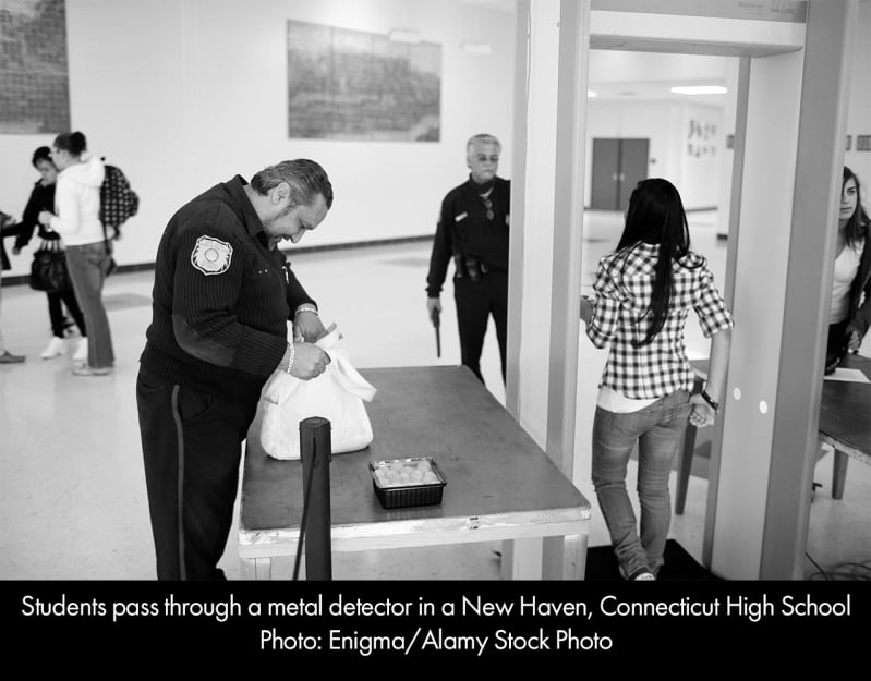A uniformed school security officer searches a bag as a student passes through a metal detector in a New Haven, Conneticut High School.